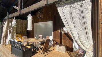 Une terrasse en bois avec une table ronde et des chaises, un banc et un panier en osier.