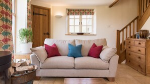 A cozy living room with a beige sofa, a wooden chest of drawers, a potted plant, and a window with a decorative valance. - Cottage 1 - sleeps 4 guests  in 2 bedrooms (New Yatt)
