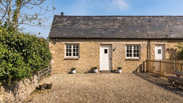 A stone cottage with a gravel driveway, a wooden fence, and potted plants. - Cottage 1 - sleeps 4 guests  in 2 bedrooms (New Yatt)