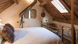 A cozy attic bedroom with a sloped ceiling, a skylight, a bed with a colorful knitted blanket, a bedside lamp, and a small round mirror. - Cottage 1 - sleeps 4 guests  in 2 bedrooms (New Yatt)