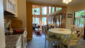 A kitchen with a microwave, a sink, and wooden cabinets. There is a dining area with a table and chairs, and a sofa in the background. - SPECTACULAR LAKEFRONT HIDEOUT RESORT-A/C- SWIM+ GOLF-KAYAK-ROWBOAT-BEACH (Hamlin)