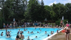 A swimming pool with people enjoying the water, surrounded by trees and a covered area. - SPECTACULAR LAKEFRONT HIDEOUT RESORT-A/C- SWIM+ GOLF-KAYAK-ROWBOAT-BEACH (Hamlin)