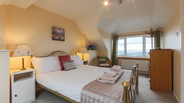 Een slaapkamer met een bed, nachtkastjes, een lamp, een stoel, een kledingkast en een raam met uitzicht.