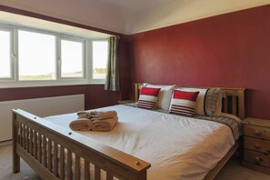 A bedroom with a bed, a wooden headboard, a nightstand, and a window with curtains.