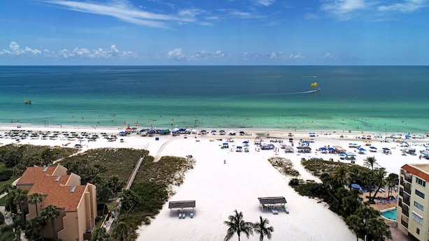 A beach with a clear view of the ocean, beach umbrellas, and a few buildings in the background. - Beautiful Siesta Key Condo (Siesta Key)