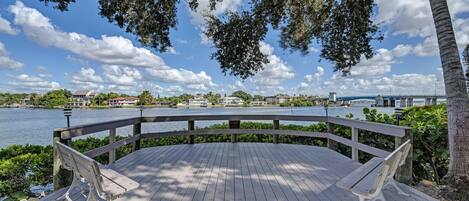 A wooden deck with benches, overlooking a body of water with a bridge in the distance.
