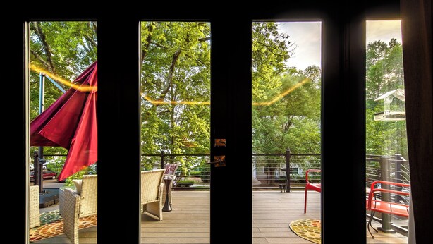 A view through a window of a deck area with outdoor furniture and a red canopy. - Charlotte Cityscape Studio, Huge Deck, Stunning View (Charlotte)