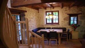A rustic dining area with a wooden table, chairs, and a bench. A staircase with wooden railings leads to an upper level. - Apartment in Dependance of a hunting lodge from the 14th century (Busserolles)