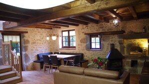 A rustic interior with a stone wall, wooden beams, a fireplace, a dining area, and a sofa. - Apartment in Dependance of a hunting lodge from the 14th century (Busserolles)