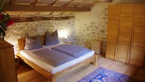 A bedroom with a wooden bed, stone walls, and a wooden wardrobe. - Apartment in Dependance of a hunting lodge from the 14th century (Busserolles)