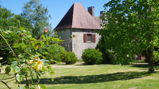 A stone building with a steeply pitched roof, surrounded by lush greenery and a well-maintained lawn. - Apartment in Dependance of a hunting lodge from the 14th century (Busserolles)