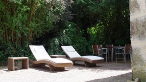 Two wicker lounge chairs with white cushions, a small table, and a set of chairs in a garden area with dense greenery in the background. - Apartment in Dependance of a hunting lodge from the 14th century (Busserolles)