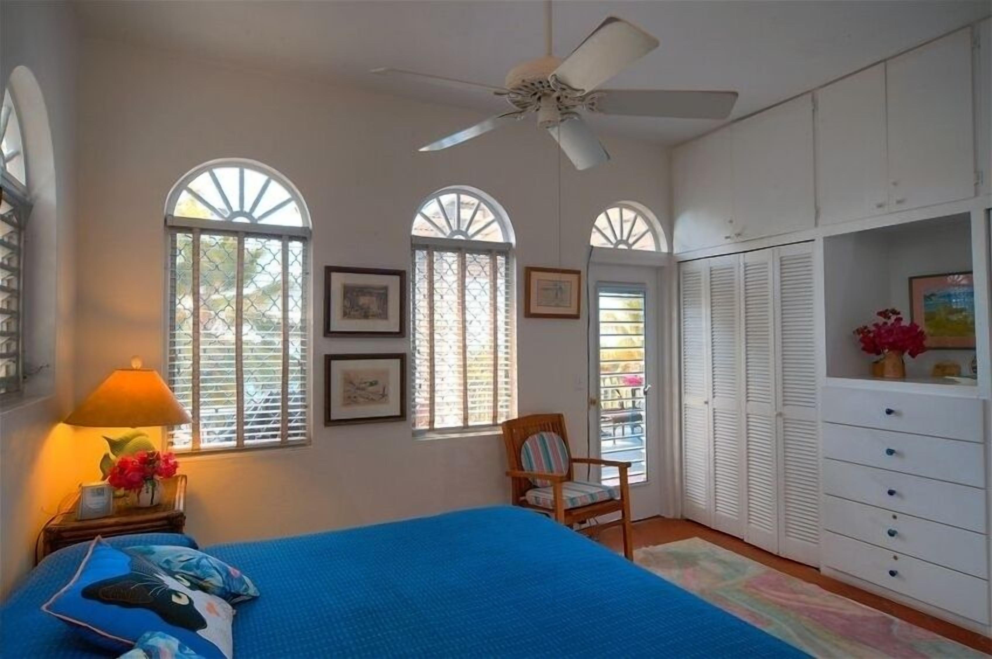 A bedroom with a bed, a chair, a wardrobe, and two windows with shutters.