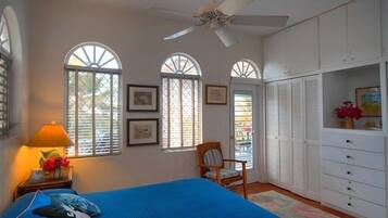 A bedroom with a bed, a chair, a wardrobe, and two windows with shutters.