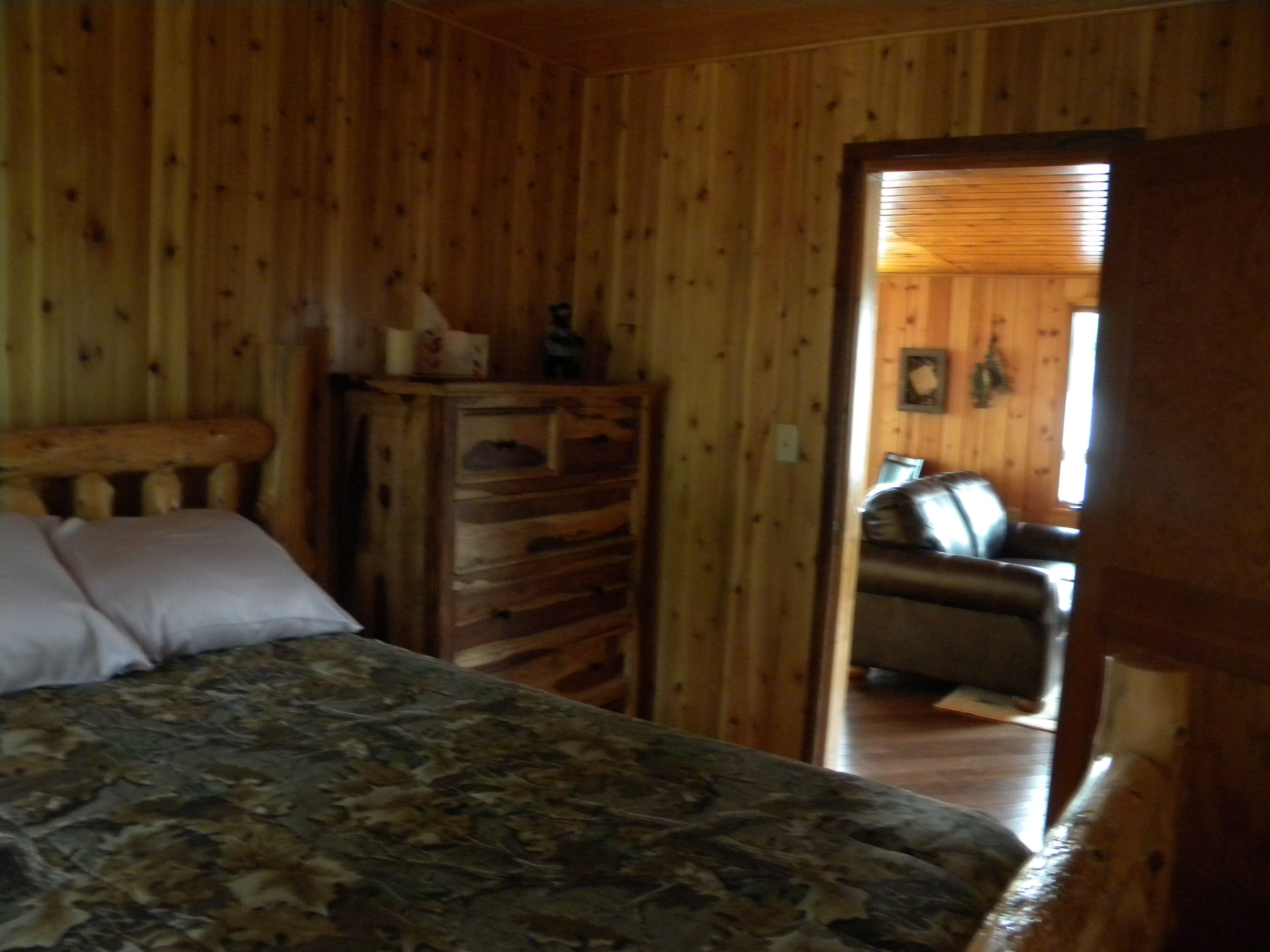 Una habitación de cabaña de madera con una cama, un aparador y vistas a una zona de estar con un sofá.