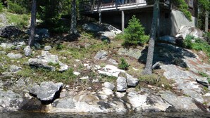 Una cabaña con terraza, rodeada de rocas y árboles, cerca de un cuerpo de agua.