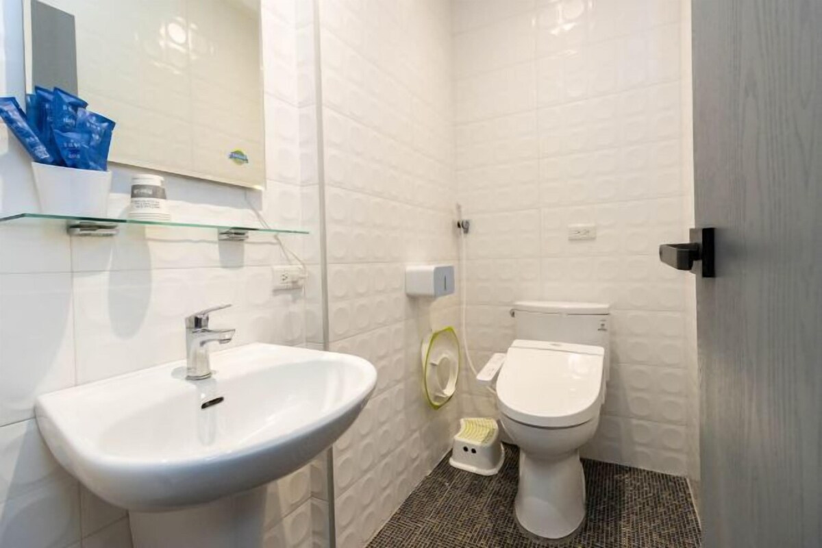 Een badkamer met een witte wasbak, toilet en een glazen plank met toiletartikelen.