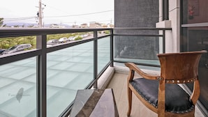 A balcony with a wooden chair, glass railing, and a view of parked cars and buildings. - Wujie Childlike B&B (Wujie)