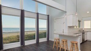 A modern kitchen with large windows overlooking a beach, wooden stools, and a granite countertop. - Beach Front on Galveston's West Beach (Galveston)
