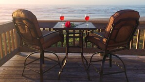 Een houten terras met twee stoelen en een tafel, met uitzicht op een strand.
