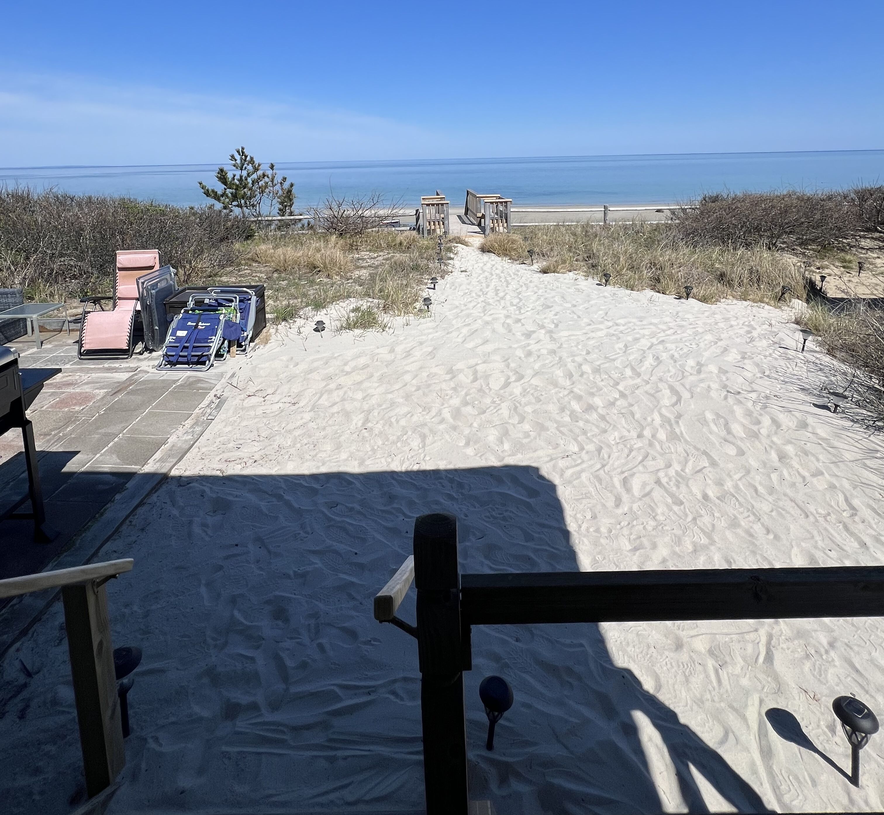 A sandy beach with a clear view of the ocean and a distant shoreline. There are beach chairs and a stroller near the water's edge.