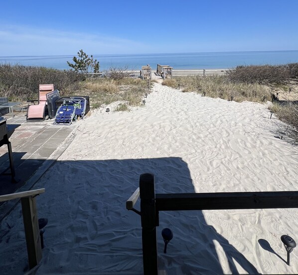A sandy beach with a clear view of the ocean and a distant shoreline. There are beach chairs and a stroller near the water's edge.