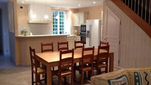 A dining area with a wooden table and chairs, a kitchen in the background, and a staircase leading to another level. - Character house, air-conditioned, heated pool, fenced garden with trees. (Villars-En-Pons)