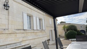 A covered outdoor area with stone walls, a pergola, and a table with chairs. - Character house, air-conditioned, heated pool, fenced garden with trees. (Villars-En-Pons)
