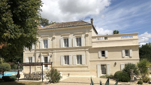 A large, two-story building with a symmetrical facade, multiple windows with shutters, and a tiled roof. - Character house, air-conditioned, heated pool, fenced garden with trees. (Villars-En-Pons)
