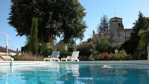 A swimming pool with lounge chairs and a large tree in the background. - Character house, air-conditioned, heated pool, fenced garden with trees. (Villars-En-Pons)