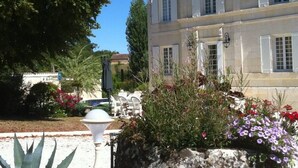 A large, two-story building with a classic architectural style, featuring multiple windows and a well-maintained garden with various plants and flowers. - Character house, air-conditioned, heated pool, fenced garden with trees. (Villars-En-Pons)