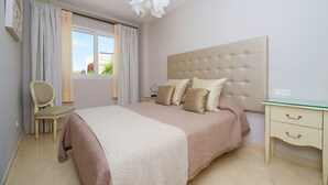 Un dormitorio con una cama grande, una mesita de noche, una silla y una ventana con cortinas.