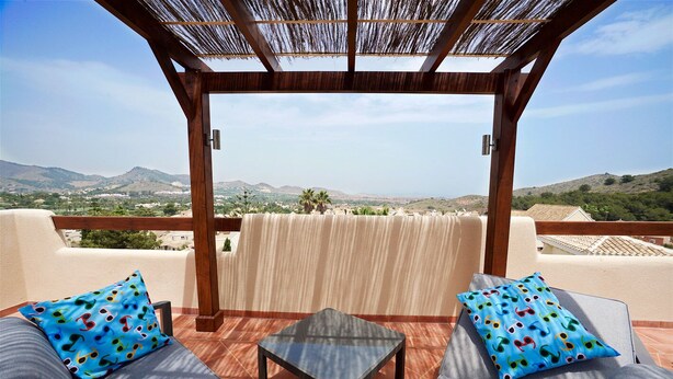 Un área de estar al aire libre con techo, con una mesa y dos sillas acolchadas, con vistas a un paisaje pintoresco.