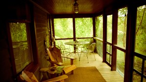 A wooden deck with a table and chairs, large windows, and a view of greenery. - Lakeside Grove Cottage -  Perfect Lakeside Village/Beach Location (Lakeside)