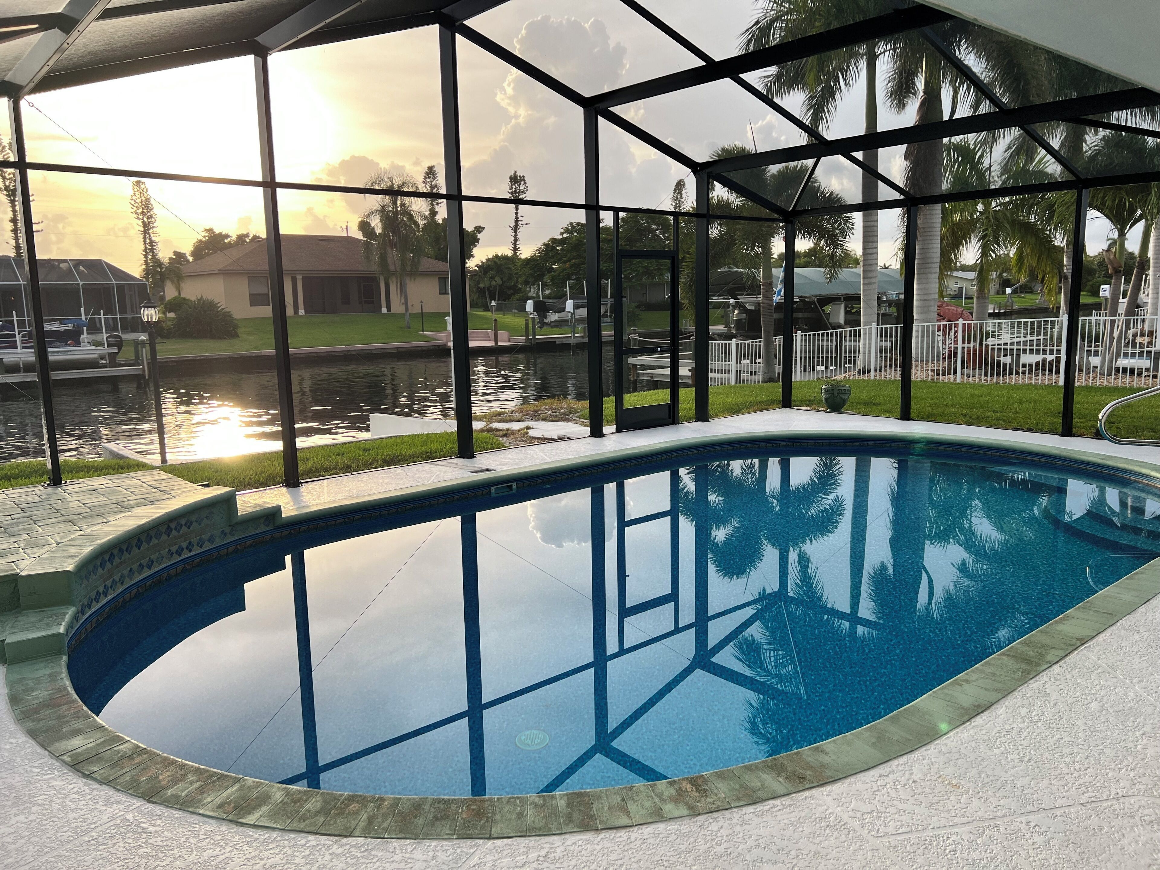 An indoor swimming pool with clear views of a sunset and a body of water outside.