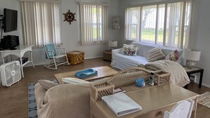 A spacious living room with a ceiling fan, a television, a sofa, a coffee table, and a wicker chair.