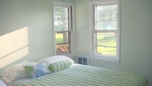 A bedroom with a bed, two windows, and a view of a lawn.
