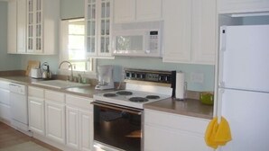 A kitchen with white cabinets, a stove, a microwave, and a refrigerator.