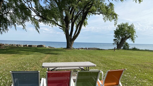 A table and four chairs set on a grassy area with a view of the sea.