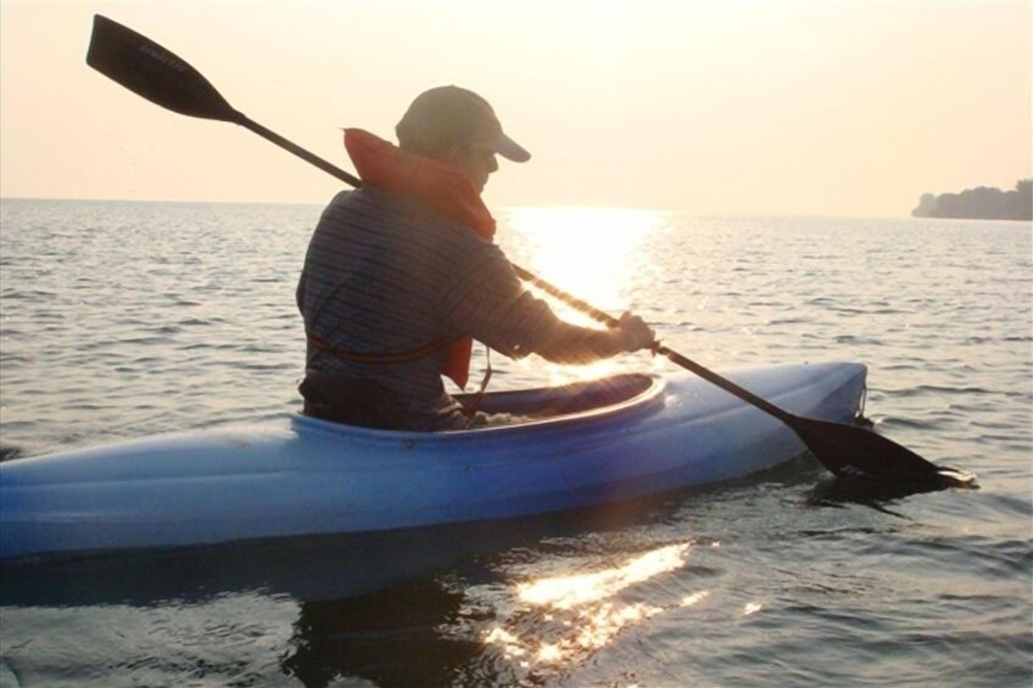 A person in a kayak on calm water during sunset.