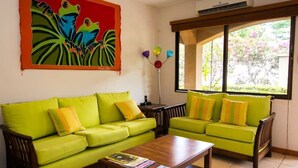Ein Wohnzimmer mit zwei grünen Sofas, einem Holztisch und einem farbenfrohen Bild an der Wand.
