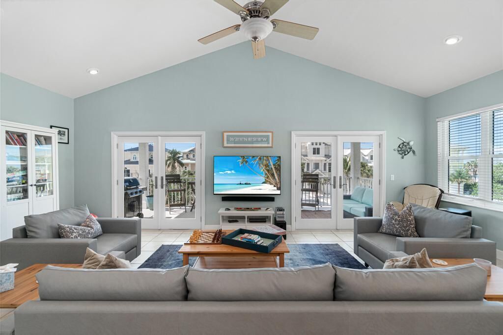 A spacious living room with a large TV, grey sofas, and a wooden coffee table.