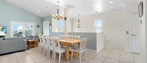 A modern kitchen with a dining area, featuring a wooden table and white chairs, a grey sofa, and a view of the outside.