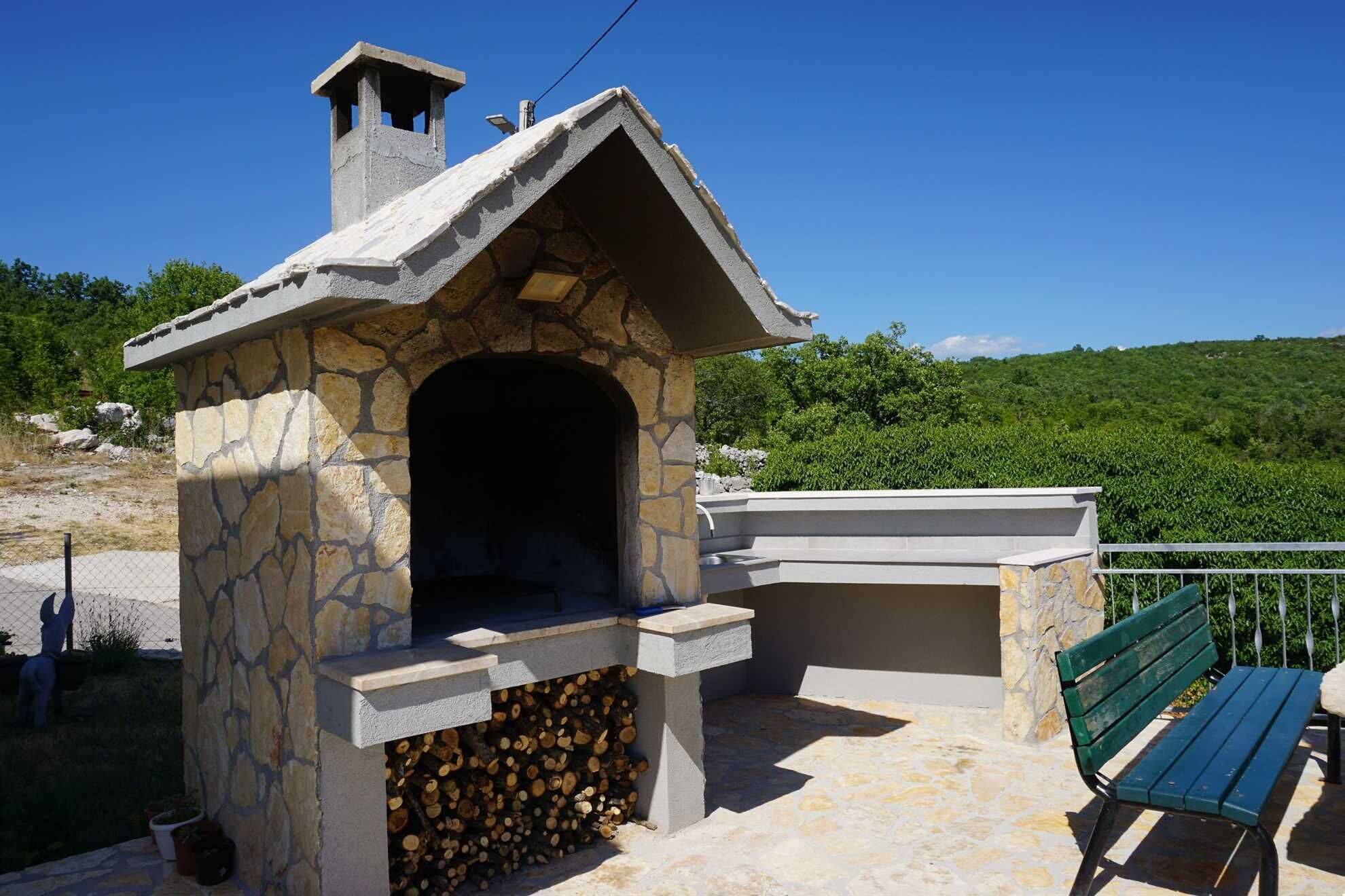 Una chimenea de piedra al aire libre con una repisa, un banco y una pila de leña.
