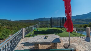 A patio with a stone table, a red umbrella, a swing set, and a view of mountains and a lake. - Holiday house Marijana (Zagvozd)