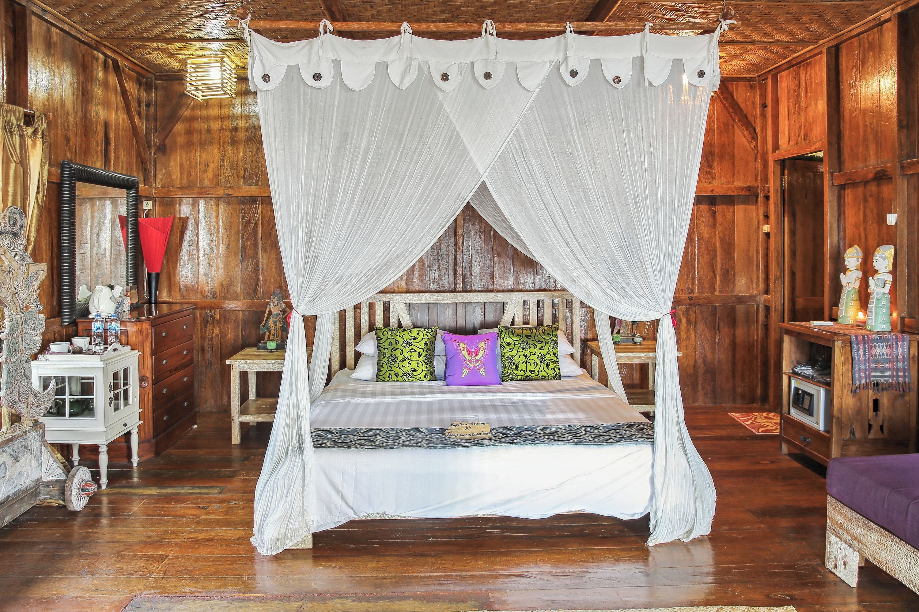A four-poster canopy bed with a white canopy, a wooden headboard, and colorful pillows.