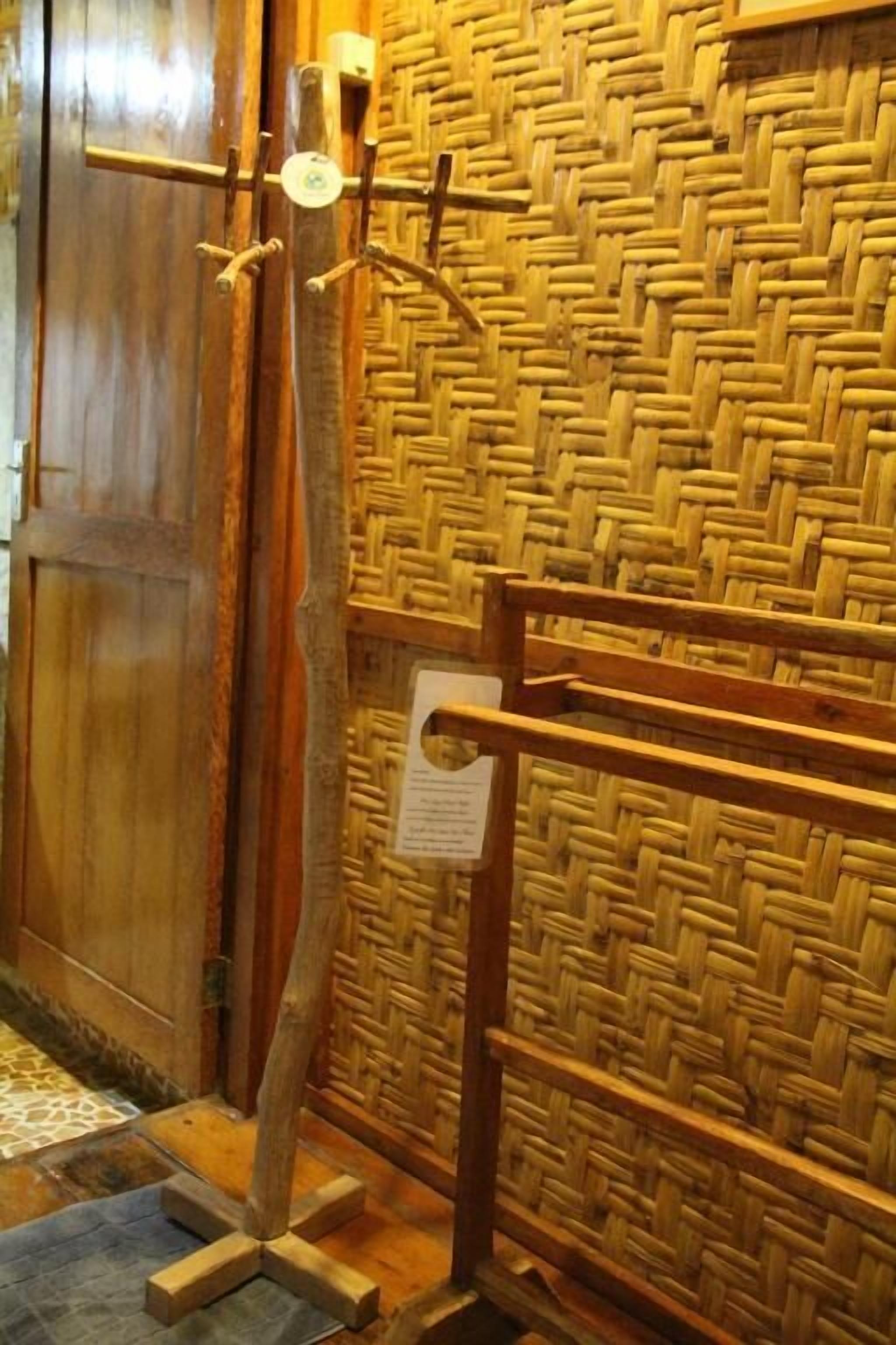 A room with a woven wall, a wooden door, and a metal rack with hooks.