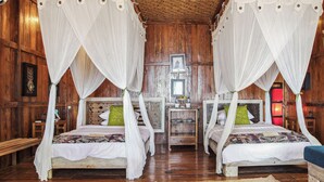Quarto com duas camas, cada uma com dossel e mesa de cabeceira. O quarto possui paredes e piso de madeira.