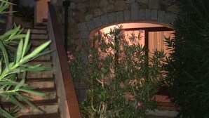 Un escalier en pierre mène à un espace abrité, doté d’un mur en pierre et d’une porte en bois.