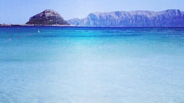 Un paysage côtier avec une eau turquoise claire et un promontoire rocheux à l’horizon.